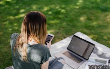 Teenager on phone using a laptop outdoors. image link to story
