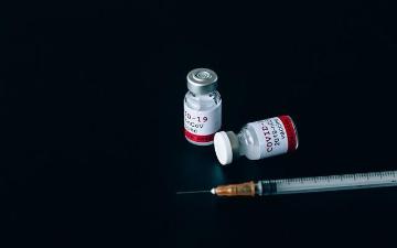 Two COVID-19 vaccine vials and a syringe on a black background. image link to story