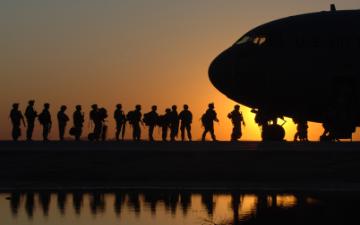Silhouettes of people boarding a military plane at sunset. image link to story