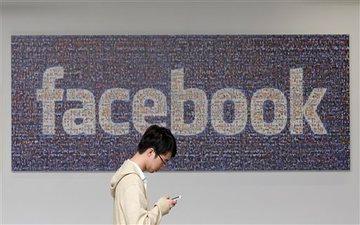 Person using phone in front of large Facebook sign.