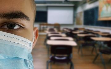 Teacher wearing face mask with rows of empty classroom chairs.