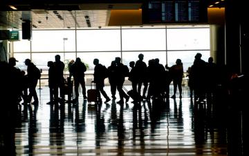 Silhouetted travelers with luggage walking through an airport. image link to story