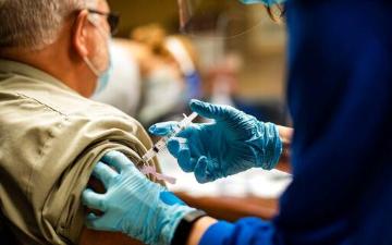 Person receiving a vaccine injection in their upper arm by a healthcare worker. image link to story