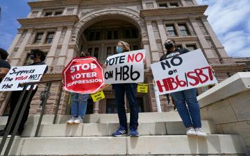 People holding signs protesting against the voter bill on a buildings steps. image link to story