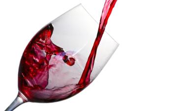 Red wine being poured into a glass on a white background. image link to story