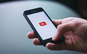 A hand holds a phone displaying the YouTube logo. image link to story