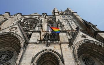 A rainbow flag is hanging on the side of a church building. Photo by Bertrand Colombo on Unsplash.