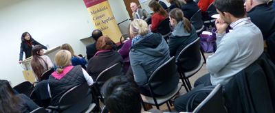Audience listening to a woman speaking at an event titled