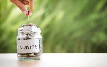 Hand putting coin into donation jar.