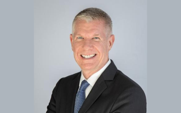 A person in a suit smiling against a light gray background. image link to story