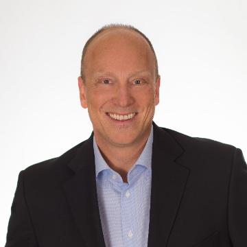 A man smiling in a dark suit jacket and light shirt.