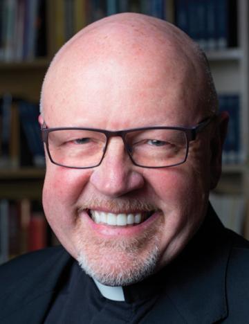 A man in glasses and clerical attire smiling.