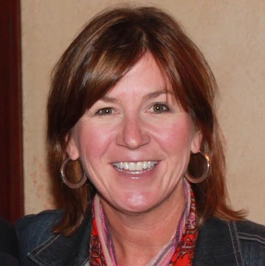 A person smiling, wearing a scarf and large hoop earrings.