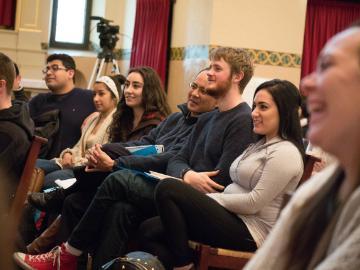People seated in a room, some smiling and attentive.