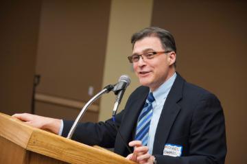 A person speaking at a wooden podium with a microphone.