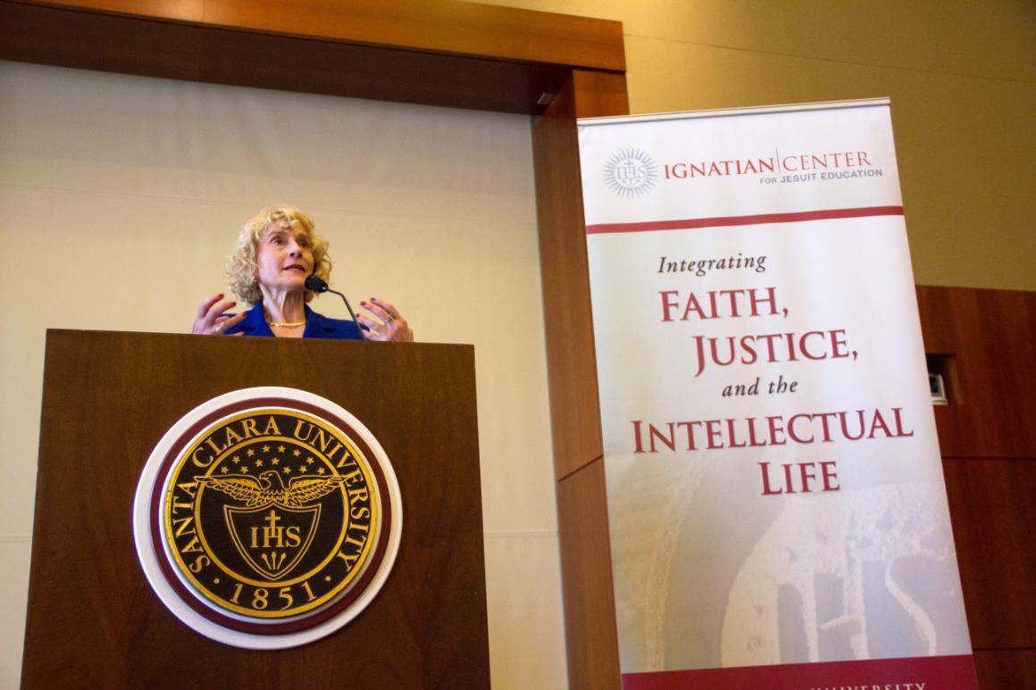 Martha Nussbaum speaking at a podium next to a 'Center for Study of World Religions' banner.