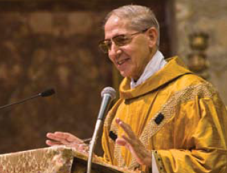 An elderly man in golden religious robes speaks at a lectern.