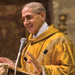 A priest in golden vestments speaking at a microphone.