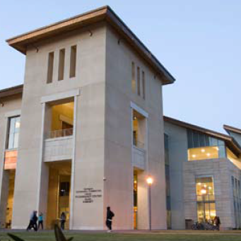 A large modern building with tall windows and people outside at dusk.