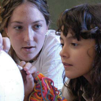 Two people closely observing an object, one holding colorful yarn.
