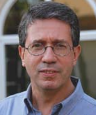 A person wearing glasses and a blue shirt in front of a building.