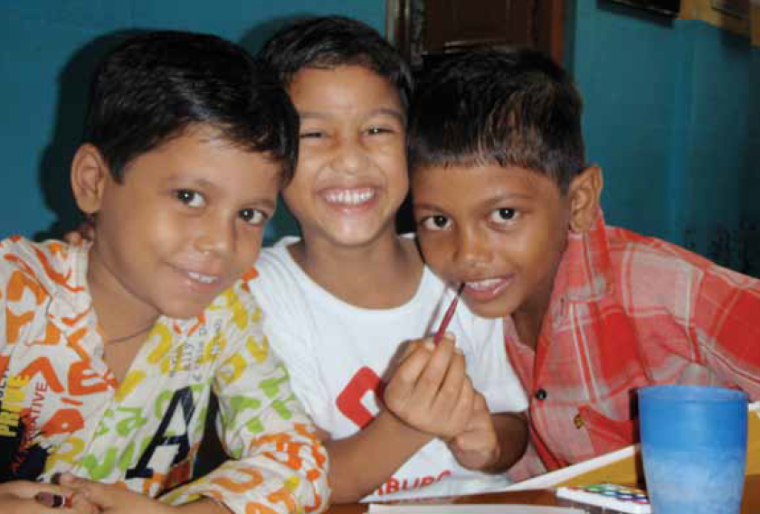 Three children smiling around a table with books and a blue cup.