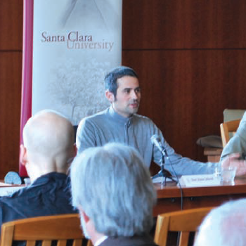 A person speaking at a table in a formal setting.