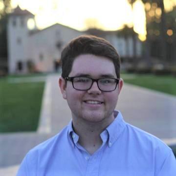 A person smiling outdoors wearing glasses and a blue shirt. image link to story