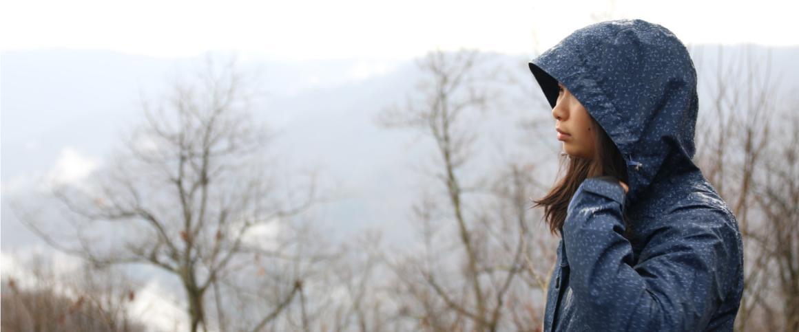 A person in a hooded jacket outdoors with bare trees in the background.