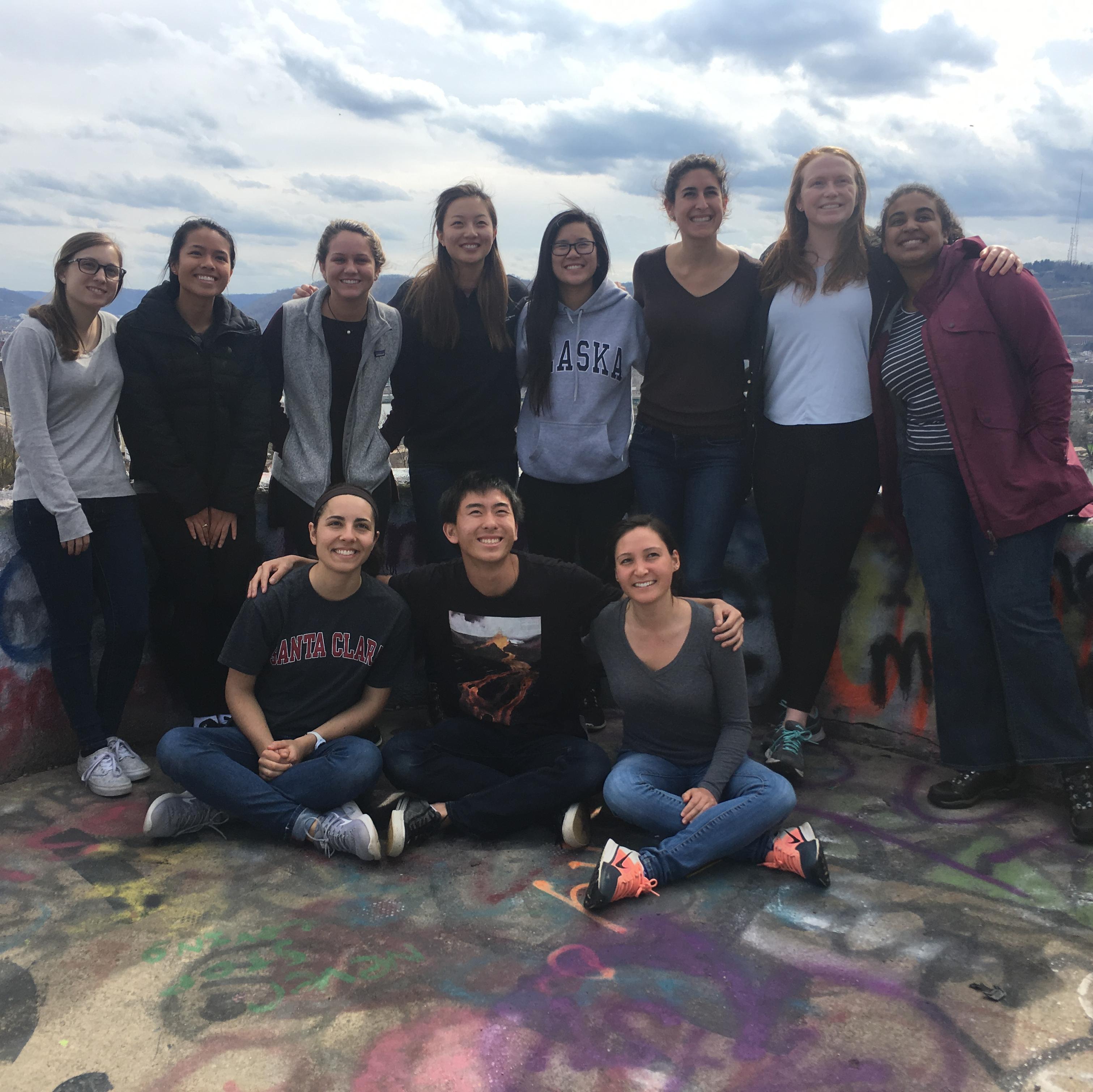 Group of people posing outdoors with a scenic, mountainous background. image link to story