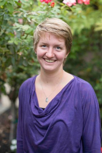 A person in a purple top smiling outdoors.
