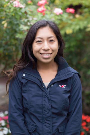 Woman in a black jacket smiling in a garden.