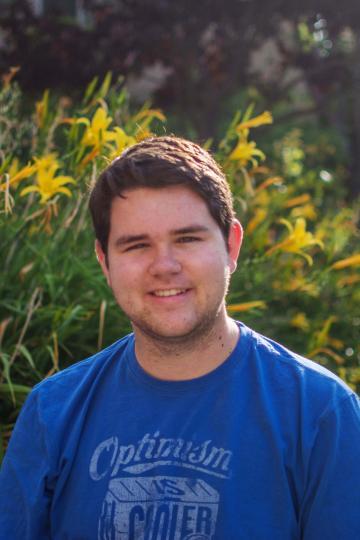 A person in a blue shirt standing in front of green foliage.