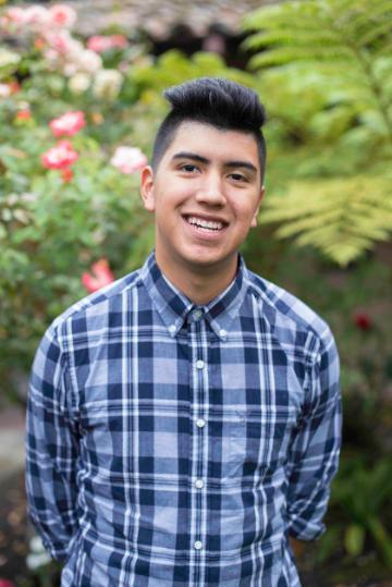 Person in a blue checkered shirt smiling in a garden.