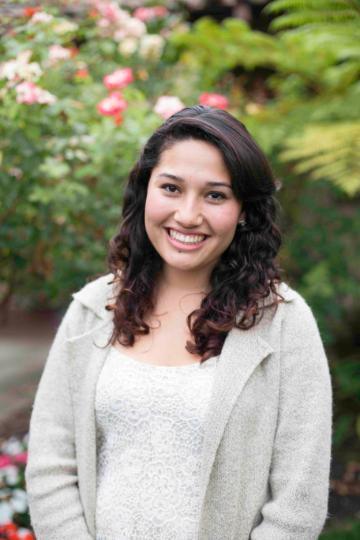 A person smiling in a garden with flowers and greenery.