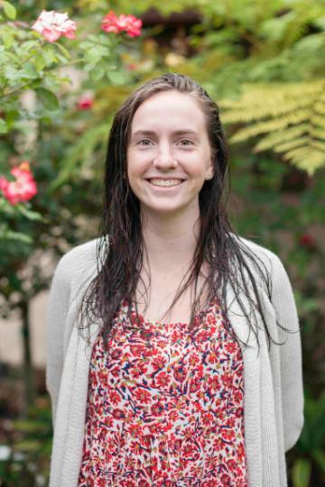 A person smiling in a garden with pink flowers.