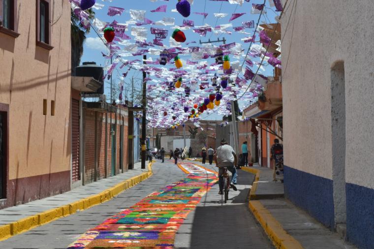 A street with floating umbrellas above, colorful murals, and pedestrians.