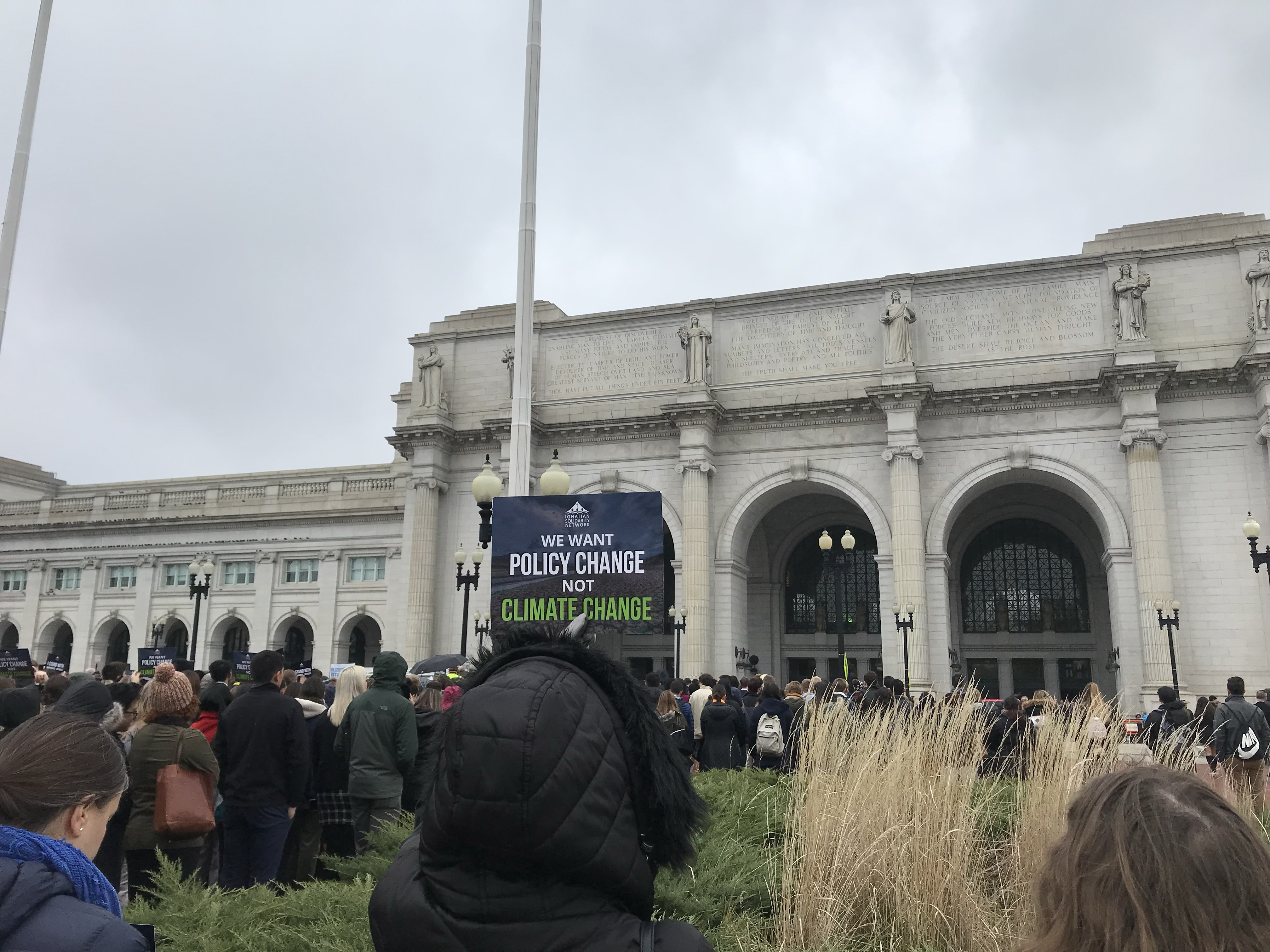 People gathered outside a large building holding a sign reading 