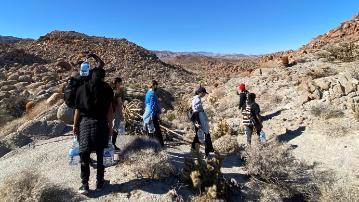 A group of hikers in a rocky desert landscape with mountains.