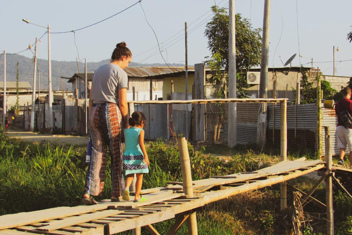 Woman and child walking on wooden bridge in a rural area.