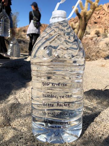 Clear water bottle labeled San Diego Immersion outdoors, with people in the background.