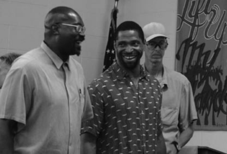 Three people smile together in a room with artwork on the wall.