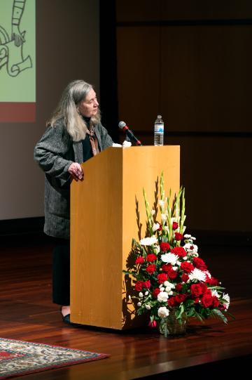 Person speaking at a podium adorned with flowers during a lecture.