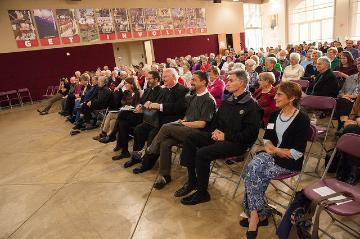 Audience seated in a hall attentively listening to a presentation.