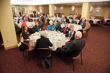 People seated at round tables in a formal dining setting.