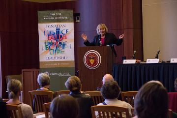A speaker addresses an audience at a podium in a meeting room.
