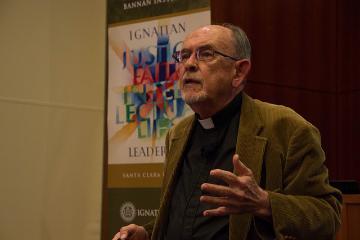 An individual gesturing during a speech with colorful artwork in the background.