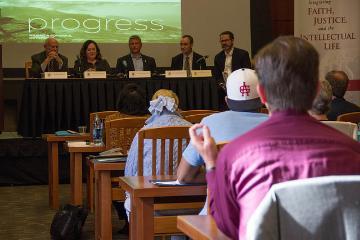 People seated in a conference room watching a panel of speakers.