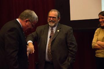 Three people interacting; one man is bowing while the other two smile.