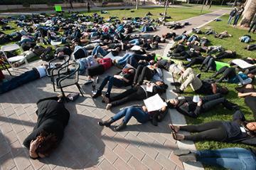 People protesting, lying on the ground in a park, some holding signs.